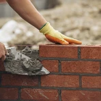 Construction worker laying red brick with trowel and mortar