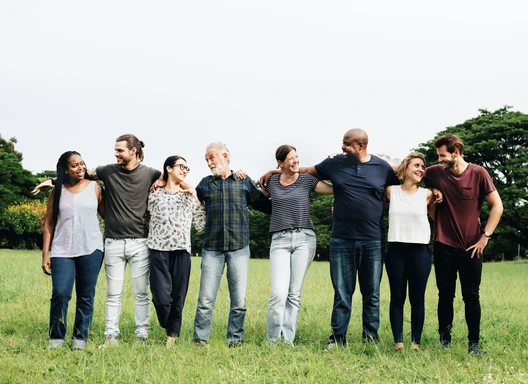 A group of adults from many different backgrounds stand together with arms linked