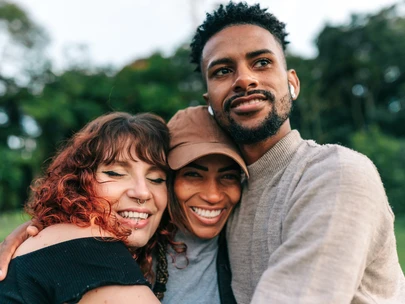 Three young adult friends hugging together in a park